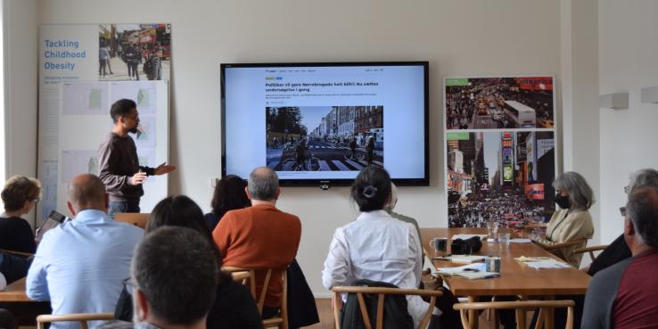 Group of participants from the SPUR study trip watch a presentation on car-free Copenhagen in a brightly lit room with wooden furniture and posters